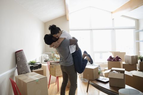 Casal entusiasmado e afetuoso, abraçando-se em nova casa, desembalando caixas de papelão